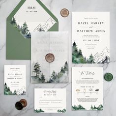 wedding stationery with mountains and trees on the front, green envelopes, and white cards