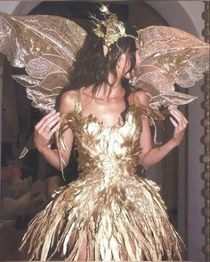 a woman in a gold dress with wings on her head