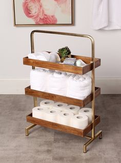 three tiered wooden rack with white towels and toilet paper on it in front of a painting