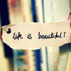 a torn piece of paper with the words life is beautiful written on it in front of bookshelves