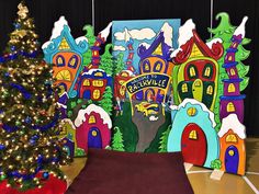 a decorated christmas tree in front of a brightly colored backdrop with houses and trees on it