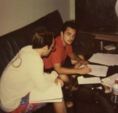 two young men sitting on a couch looking at papers and pens in front of them