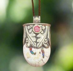 a silver vase hanging from a cord with a red bead on it's end