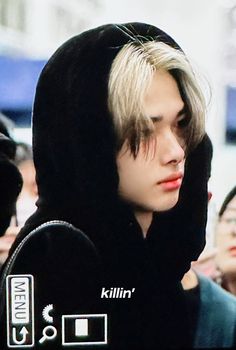 a man with blonde hair wearing a black hoodie and looking at his cell phone