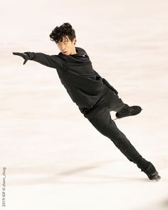 a young man skating on an ice rink wearing black clothes and holding his arms out in the air