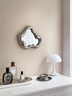 a mirror on the wall above a table with perfumes and an alarm clock next to it