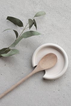 a wooden spoon sitting on top of a white bowl next to a leafy branch