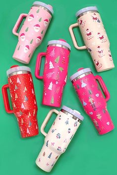 six different colored coffee mugs sitting on top of a green surface with christmas trees and snowflakes