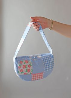 a hand holding a blue and white patchwork purse with flowers on the front pocket