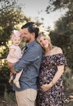 a man and woman holding a baby in their arms while standing next to each other