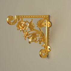 an ornate gold brooch with flowers and leaves on it's side, hanging from a wall