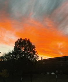 an orange and pink sky at sunset with trees in the foreground