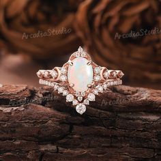 a white opal and diamond ring on top of a tree branch in front of some rocks