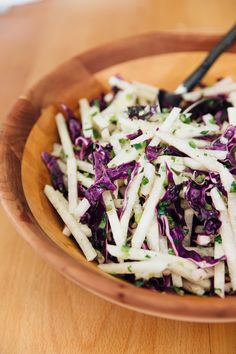 a wooden bowl filled with coleslaw on top of a wooden table next to a fork