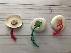 three hats with string attached to them on a white wooden surface, one is red and the other two are green