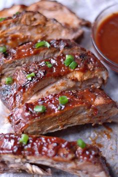 some ribs with sauce and green onions on them sitting on a piece of parchment paper next to a bowl of ketchup