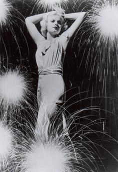 an old black and white photo of a woman standing in front of fireworks