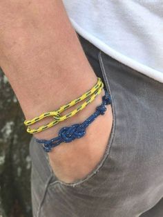 a person wearing two bracelets with blue and yellow cords on their wrist, both tied together