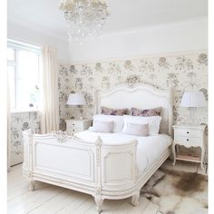 a white bed sitting in a bedroom next to a window with a chandelier