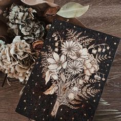 a wooden card with flowers on it next to some pine cones and dried leaves in the background