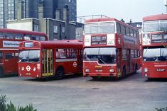 three red double decker buses parked next to each other in a parking lot with tall buildings behind them