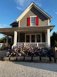 a gray house with red shutters and flowers in front