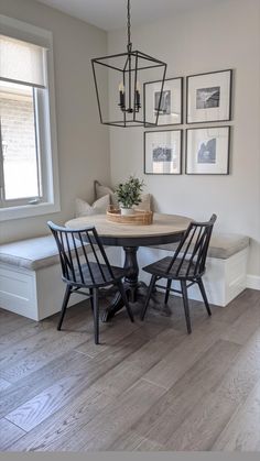 a dining room table with four chairs and a bench in front of the window that has pictures on the wall above it