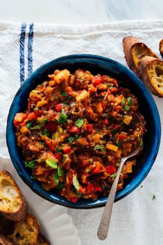 a blue bowl filled with food on top of a white cloth next to sliced bread