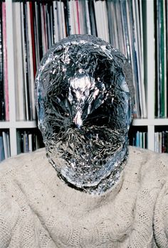 a man wearing a silver foil covering his face in front of a book shelf filled with books