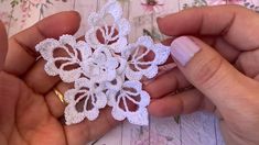 two hands holding white crochet flowers on a table