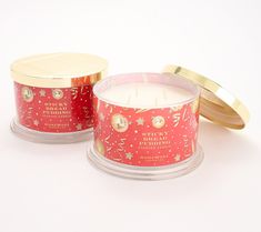 two red candles sitting next to each other on a white surface with gold trimmings