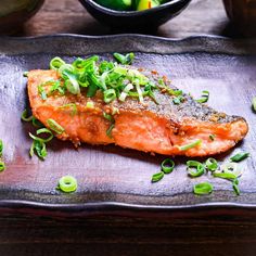 a piece of salmon with green onions and scallions on a black platter