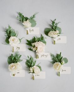 wedding boutonnieres with white flowers and greenery are arranged on a wall