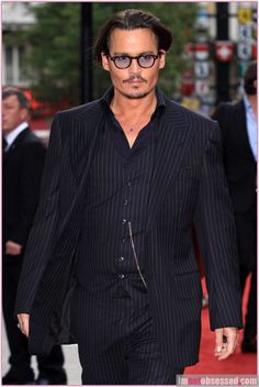 johnny beck walks down the red carpet in his suit and tie, while wearing glasses