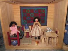 two dolls are sitting in a dollhouse with furniture and quilts on the walls