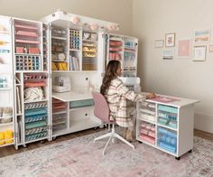 a woman sitting at a desk in front of a white cabinet with lots of crafting supplies