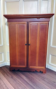 a wooden cabinet sitting on top of a hard wood floor next to a wall with white paneling