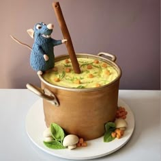 a cake made to look like a pot of soup with a mouse on top and carrots around it