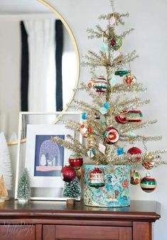 a small christmas tree with ornaments on it and a mirror in the corner behind it