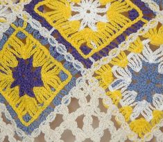 a crocheted tablecloth with yellow and blue squares on the top, along with white doily