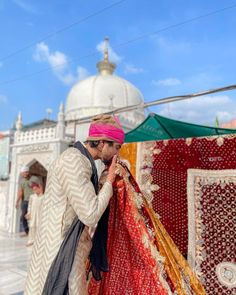 a man in a pink turban standing next to a red and white rug