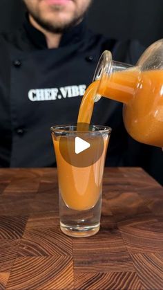 a man pouring orange juice into a glass on top of a wooden table next to a cup