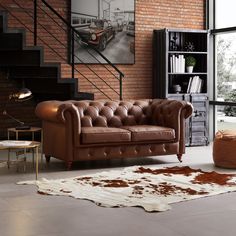 a brown leather couch sitting in front of a brick wall next to a stair case