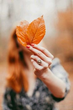 a woman holding an orange leaf in her hand