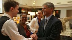 two men shaking hands with other people in the background