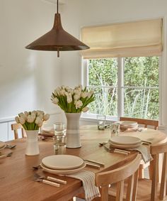 a dining room table is set with place settings and flowers in a vase on the table