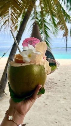 a person holding up a coconut drink with flowers on the rim and an umbrella in the background