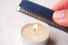 a small white candle with a zipper around it's side and a hand holding one