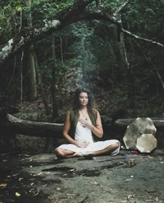 a woman sitting in the middle of a forest with her hands clasped to her chest