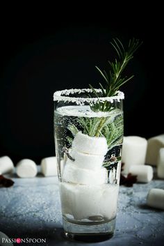 a glass filled with white marshmallows and topped with a sprig of rosemary